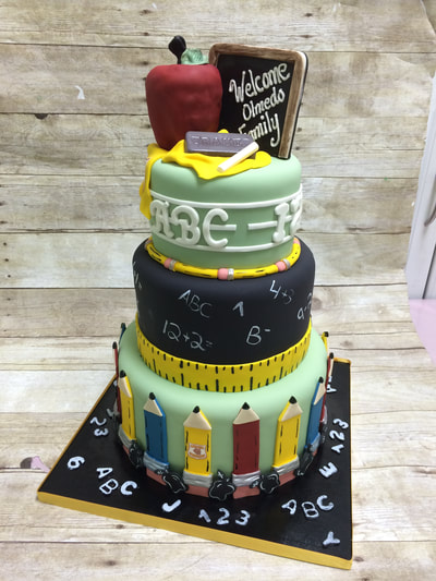 3 tier cake for a teacher. Apple and chalkboard on top of cake and alphabet writing around top tier. 2nd tier is black like a chalkboard with a ruler around the bottom, The bottom tier of cake is surrounded by flat fondant pencils.
