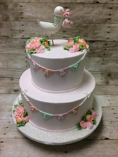 2 tier baby shower cake with a stork on top, buttercream flowers and draped flags with baby's name on them.