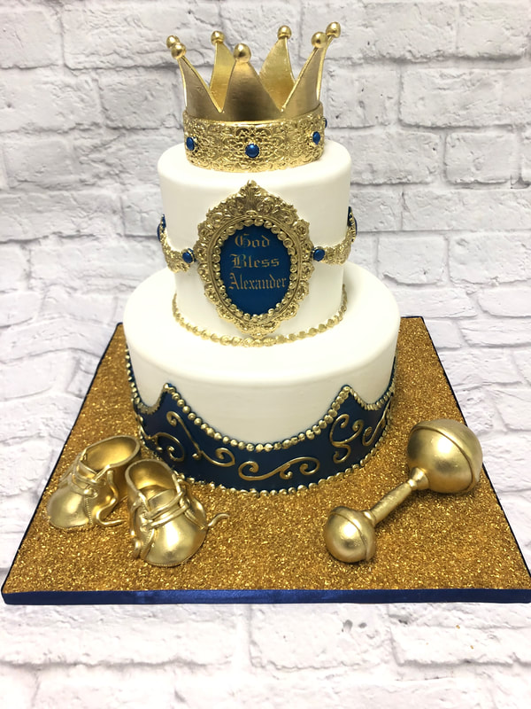baby shower cake for a boy. baby prince theme with crown on top and gold baby rattle and gold chocolate baby booties on bottom.